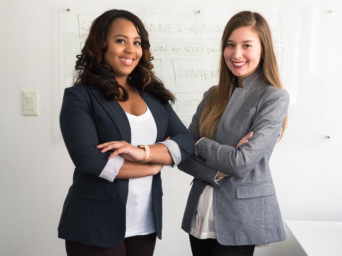 two women in suits standing beside wall